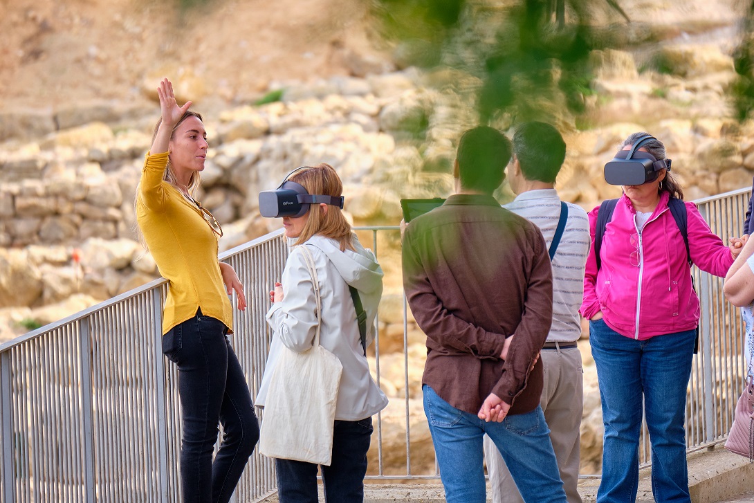 Una dona guiant un grup de visitants amb ulleres 360º en un jaciment.