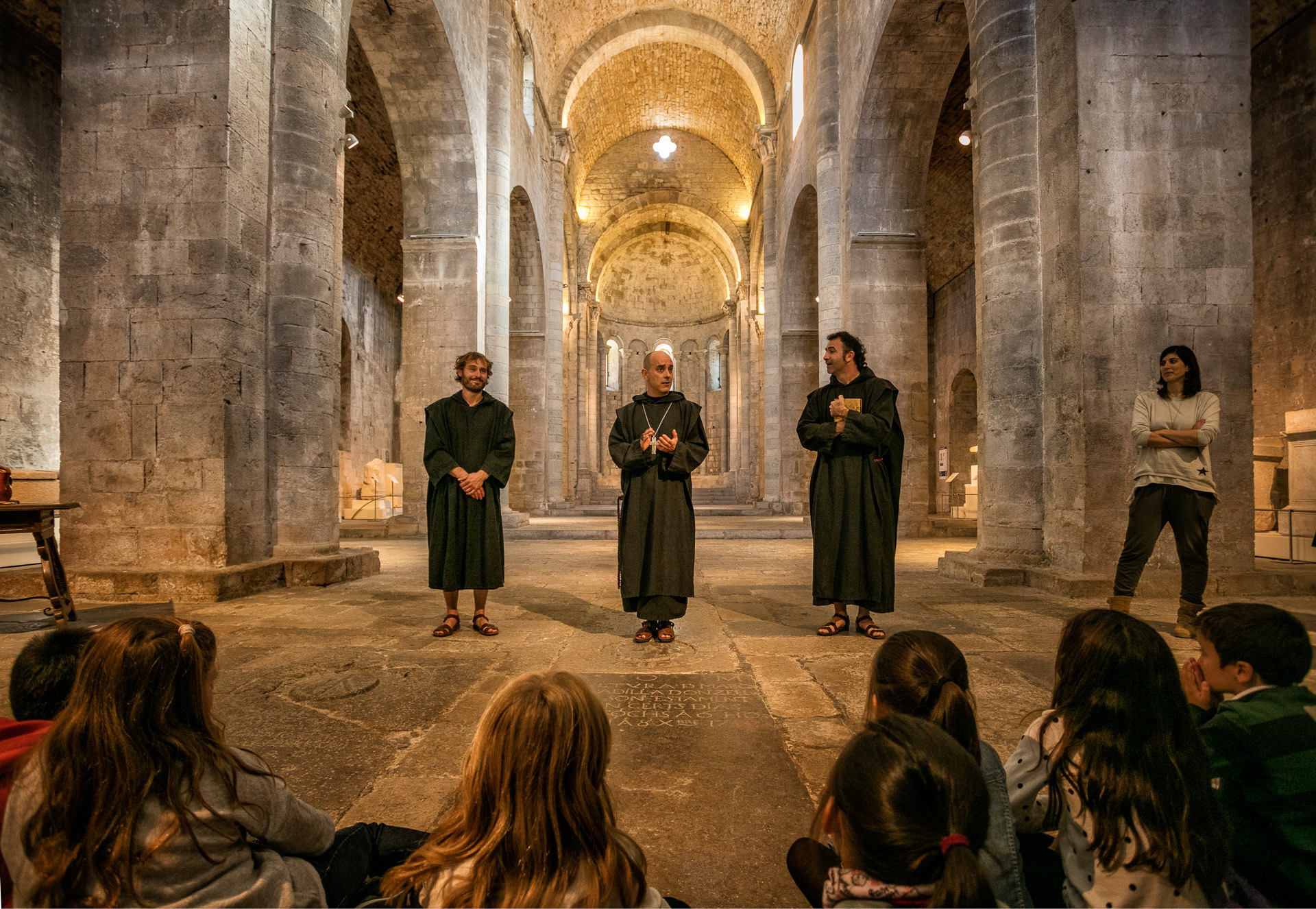 Tres monjos parlant amb infants a l'interior d'un monestir.
