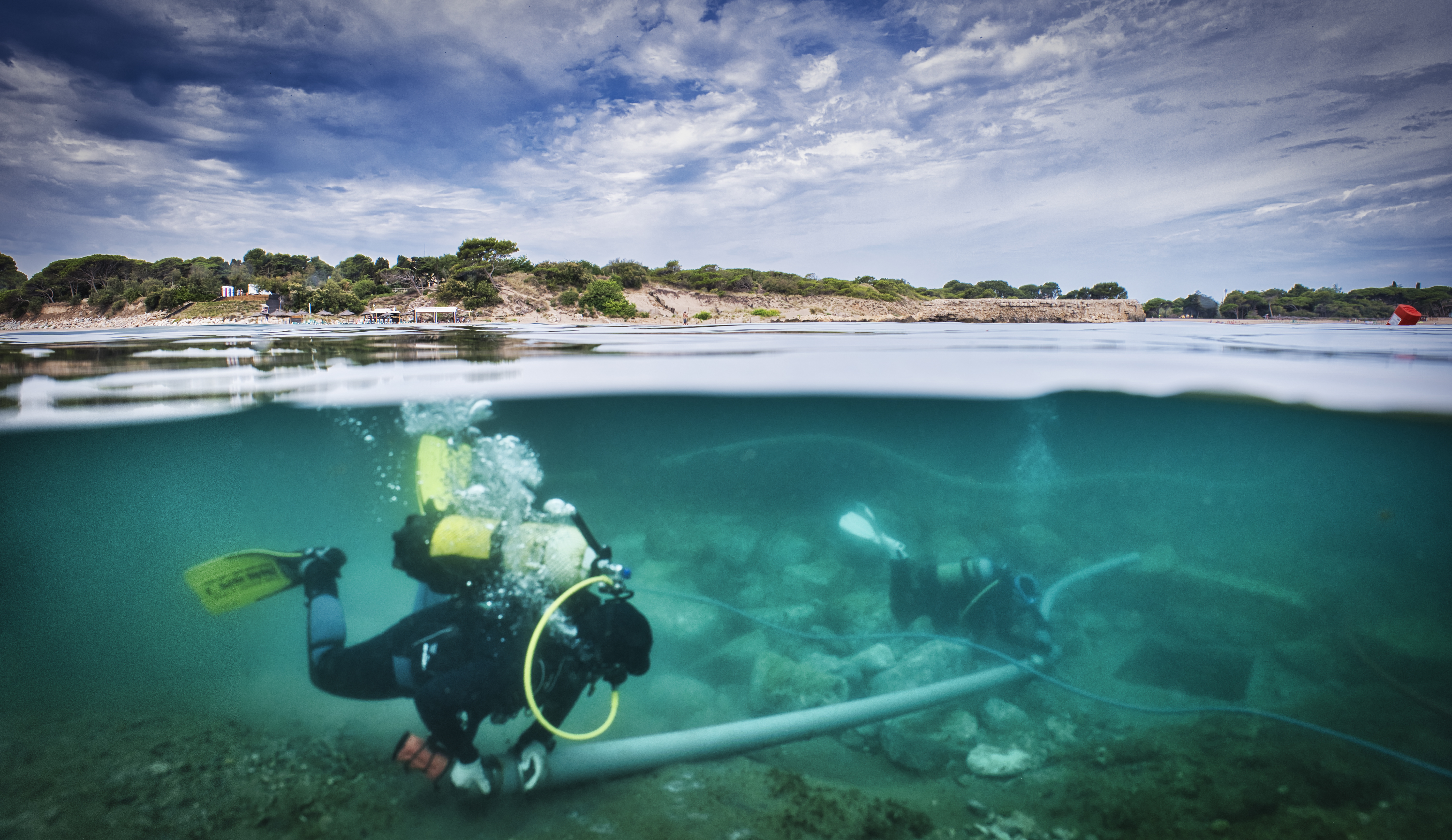 Submarinista excavant un jaciment subaquàtic amb Empúries de fons.
